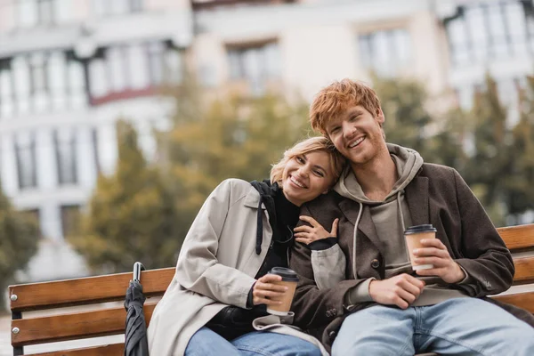 Veselá Mladá Žena Objímající Muže Drží Kávu Jít Zatímco Sedí — Stock fotografie