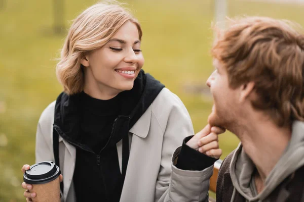 Cheerful Blonde Woman Holding Paper Cup Touching Chin Redhead Boyfriend — Stock Photo, Image