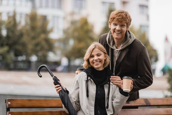 Zrzka Muž Drží Papírový Pohár Blízkosti Blondýny Žena Sedí Lavičce — Stock fotografie