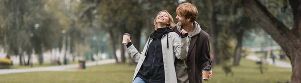 快乐的红头发男人看着快乐的女人一边拿着咖啡一边在公园里笑 一面挂着横幅 — 图库照片