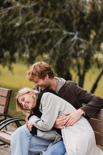 Pelirrojo Hombre Riendo Mientras Abrazando Feliz Novia Mientras Sentado Banco — Foto de Stock