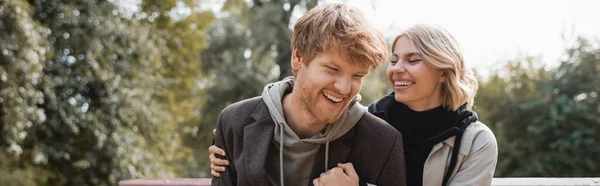 Cheerful Blonde Woman Embracing Redhead Boyfriend While Smiling Park Banner — Stock Photo, Image