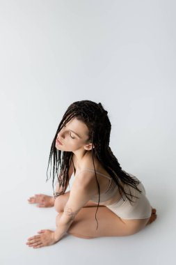 Gri arka planda oturan iç çamaşırlı dövmeli modelin genel görünümü 