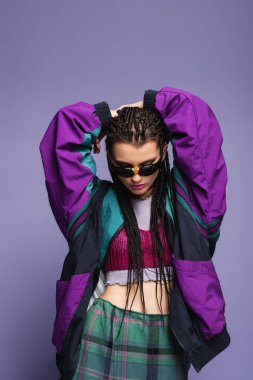 Fashionable model with braids hairstyle and retro sports jacket posing isolated on purple  clipart