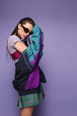 woman with braids posing in sunglasses with vintage style jacket isolated on purple clipart