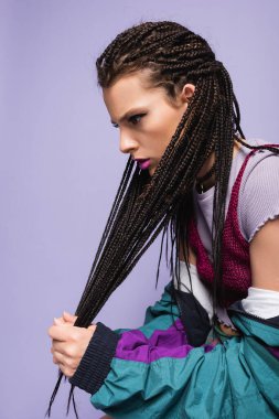 young woman in vintage clothes touching braided dreadlocks isolated on purple clipart