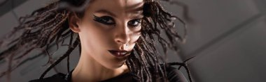 portrait of brunette woman with stylish makeup and braids looking at camera on grey background, banner clipart