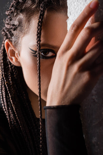 молодая женщина с футуристическим макияжем смотрит на камеру возле белой стены на черном фоне