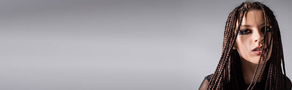портрет брюнетки с дредами и выразительным макияжем изолирован на сером, баннер