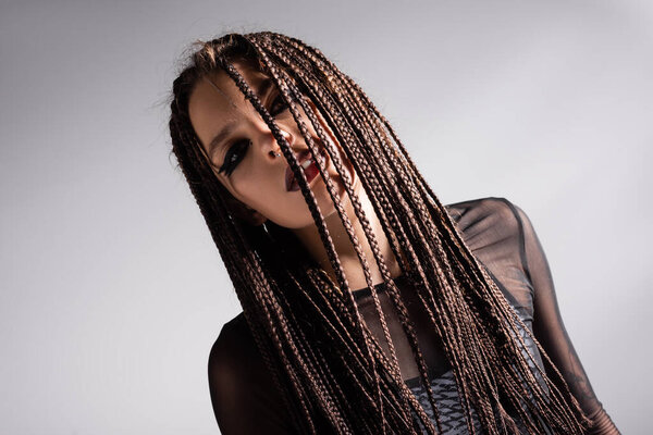 брюнетка с косичками и футуристическим макияжем позирует изолированно на сером