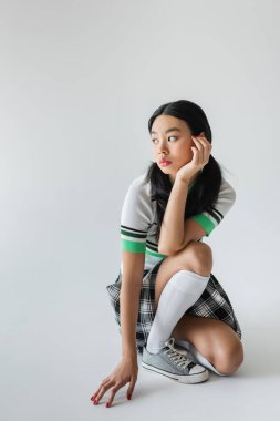 Dizlerinde çorap ve spor ayakkabıları olan modaya uyan Asyalı kadın gri arka plana bakıyor. 