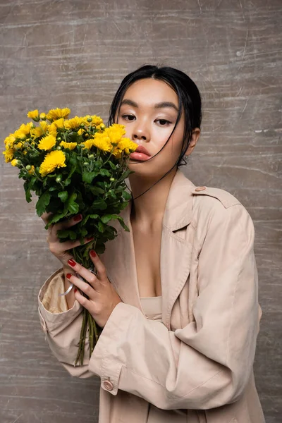 Retrato Modelo Asiático Gabardina Beige Sosteniendo Crisantemos Sobre Fondo Marrón — Foto de Stock