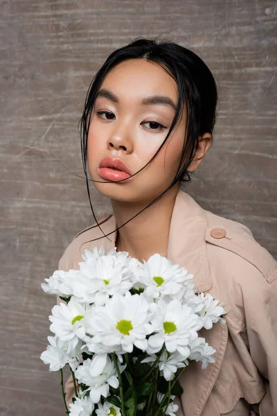 Hübsche Asiatin Trenchcoat Mit Weißen Chrysanthemen Auf Abstraktem Braunem Hintergrund — Stockfoto