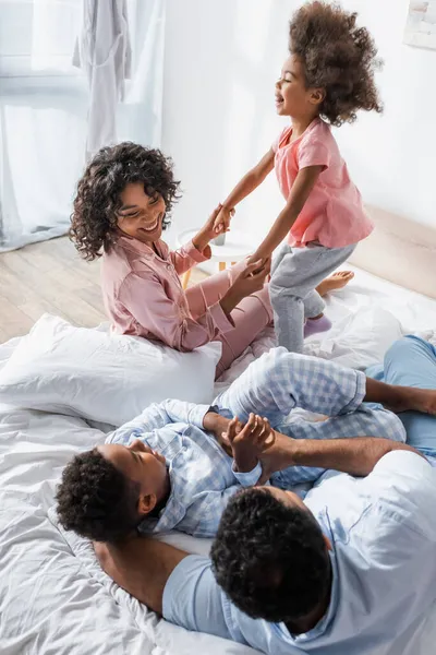 African american woman holding hands with daughter near husband hugging son in bedroom — Stock Photo