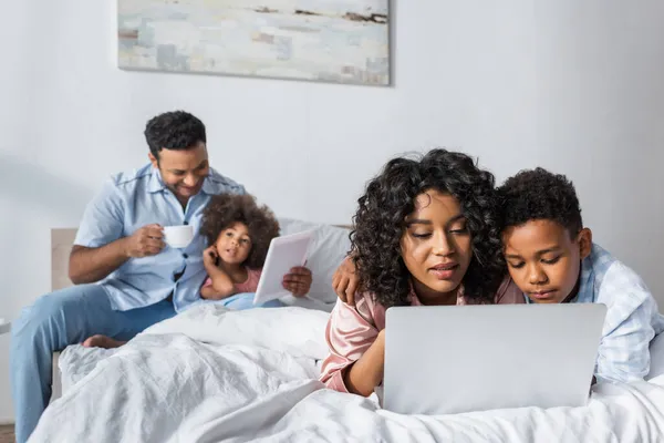 African american parents with kids using laptop and digital tablet in bedroom — Stock Photo