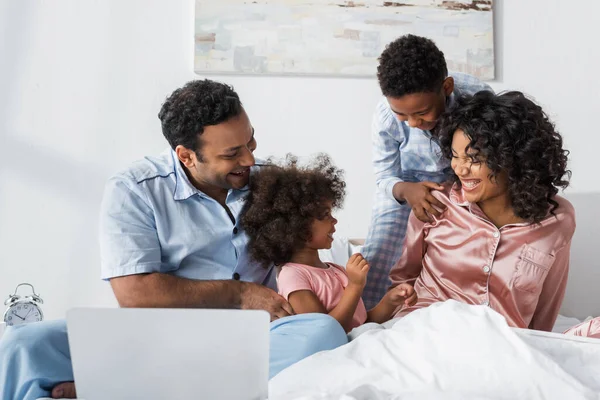 Homme afro-américain près d'un ordinateur portable et la famille joyeuse dans la chambre — Photo de stock