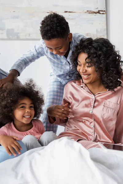 Fröhliche afrikanisch-amerikanische Frau mit Kindern im Schlafanzug hat Spaß im Schlafzimmer — Stockfoto
