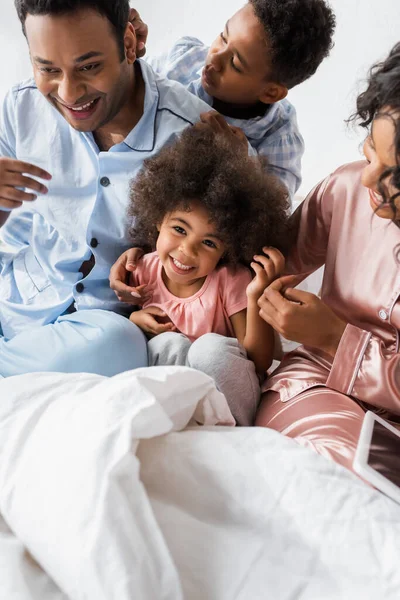 Aufgeregtes afrikanisch-amerikanisches Mädchen blickt in die Kamera, während es mit der Familie im Schlafzimmer Spaß hat — Stockfoto