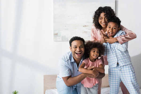 Felici genitori afro-americani che abbracciano i bambini mentre si divertono in camera da letto al mattino — Foto stock