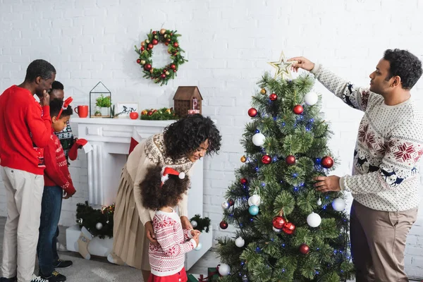 African american family decorating christmas tree and fireplace in living room — Stock Photo