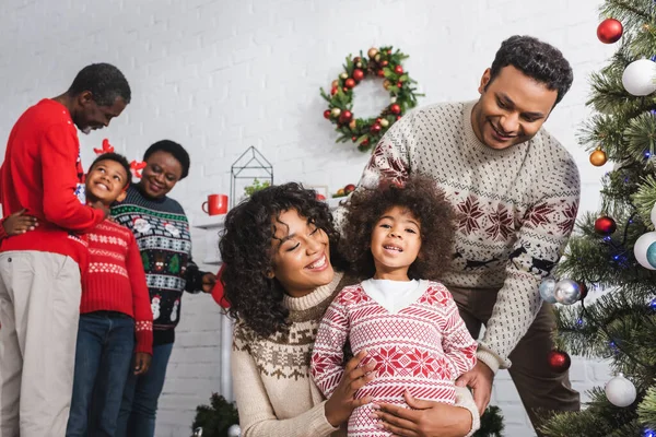 Alegre afro-americano pais abraçando filha perto filho borrado com avós na sala de estar com decoração de natal — Fotografia de Stock