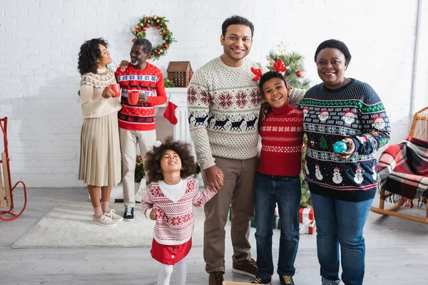 Niños afroamericanos felices cerca del padre y la abuela en la sala de estar con decoración de Navidad - foto de stock