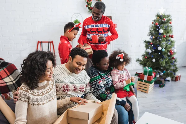 Allegro afro americano famiglia imballaggio regali in soggiorno con albero di Natale offuscata — Foto stock