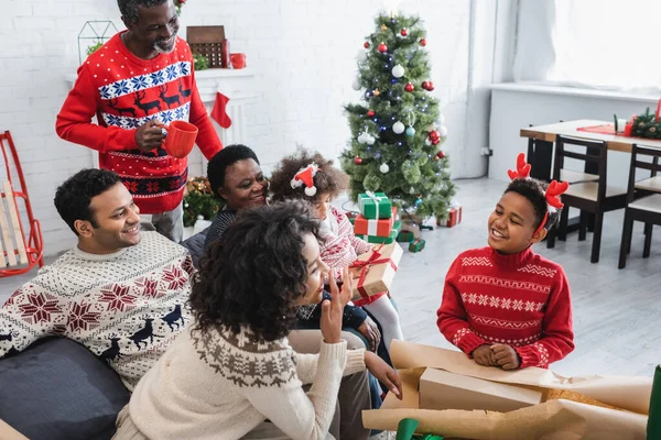 Heureux garçon afro-américain en cornes de renne headband emballage boîte cadeau avec la famille — Photo de stock