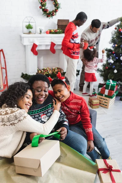 Happy african american woman and boy embracing excited granny while packing christmas present — Stock Photo