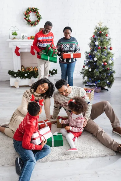 Familia afroamericana feliz con cajas de regalo en sala de estar decorada con árbol de Navidad - foto de stock