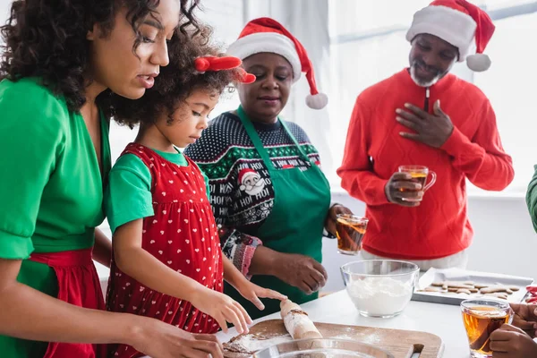 Pleased african american grandparents looking at granddaughter preparing christmas cookies with mother — Stock Photo