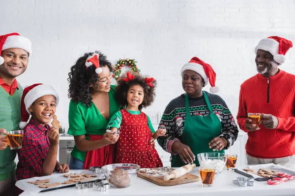 Menina feliz segurando cortador de biscoitos enquanto prepara biscoitos de Natal com a família afro-americana — Fotografia de Stock