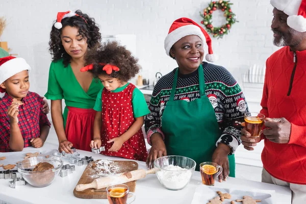 Bambini africani americani che preparano i biscotti di Natale con la madre e i nonni in cappelli di Babbo Natale — Foto stock