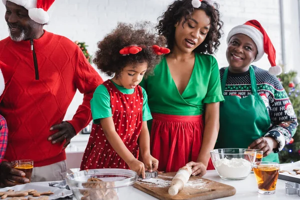 African american women and girl preparing christmas cookies near granddad standing with hand on hip — Stock Photo