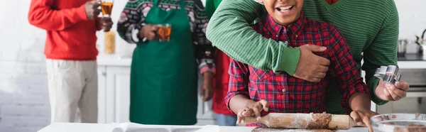 Обрізаний вид батька, що тримає різак для печива і приймає афроамериканського сина, який готує на кухні, банер — стокове фото