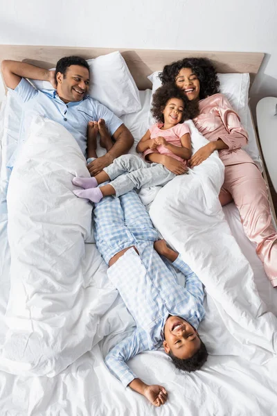 Top view of cheerful african american family laughing while lying in bed in morning — Stock Photo