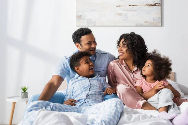 Feliz africano americano pareja hablando en cama cerca alegre niños - foto de stock