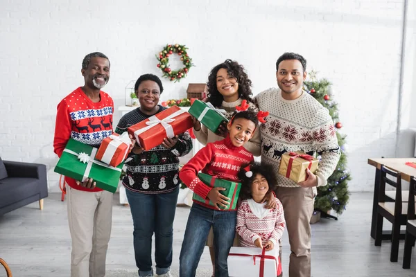 Alegre família afro-americana com presentes de Natal olhando para a câmera na sala de estar decorada — Fotografia de Stock