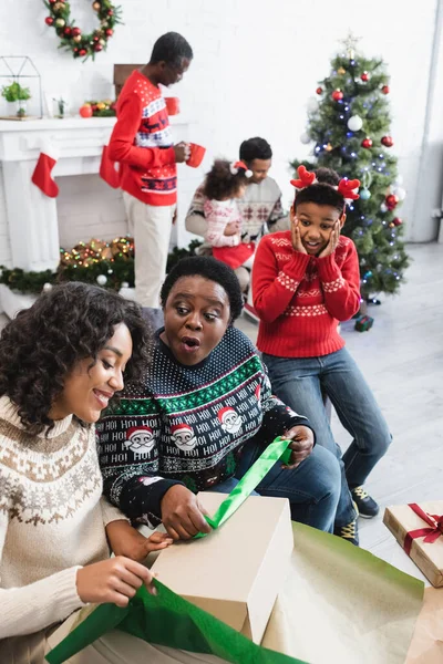 Erstaunt afrikanisch-amerikanischer Junge schaut aufgeregte Oma und Mutter beim Packen von Weihnachtsgeschenken an — Stockfoto