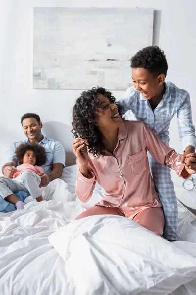 Схвильована афроамериканська мати і син розважаються в спальні біля розмитого чоловіка з дочкою — стокове фото