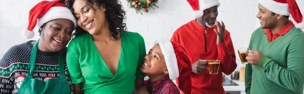 Fröhliche afrikanisch-amerikanische Frauen und Jungen neben Männern mit orangefarbenem Zimttee im Gespräch auf verschwommenem Hintergrund, Banner — Stockfoto