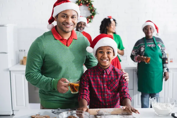 Афроамериканський чоловік з апельсиновим чаєм кориці біля розмитої сім'ї та щасливим сином, який готує на кухні — стокове фото