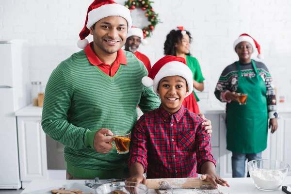 Homem americano africano com chá de canela laranja perto da família turva e filho feliz cozinhar na cozinha — Fotografia de Stock