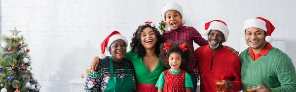 Joyeuse famille afro-américaine en chapeaux Santa regardant la caméra près de l'arbre de Noël, bannière — Photo de stock