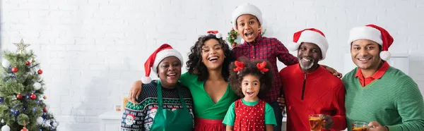 Alegre família afro-americana em santa chapéus olhando para câmera perto de árvore de natal, banner — Fotografia de Stock