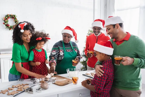 Happy african american family drinking orange cinnamon tea while preparing christmas cookies in kitchen — Stock Photo