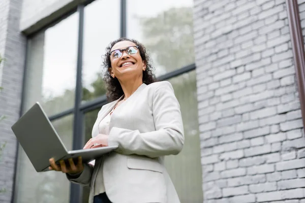 Low angle view of happy african american businesswoman using laptop outdoors — Stock Photo