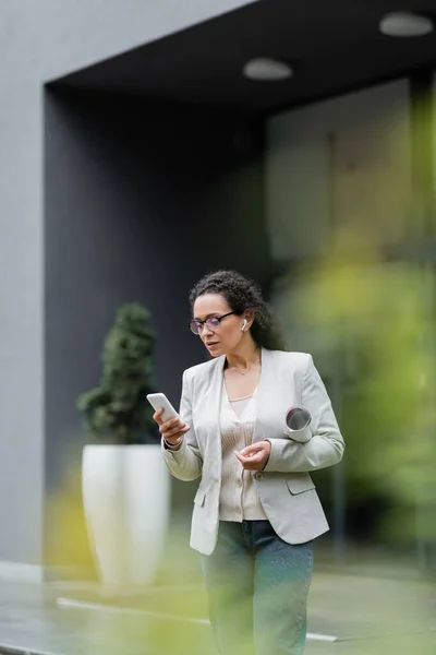 Femme d'affaires afro-américaine dans les lunettes en utilisant le téléphone mobile à l'extérieur sur le premier plan flou — Photo de stock