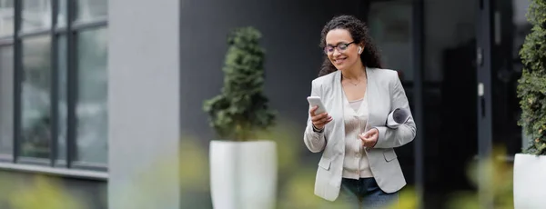 Gerente afroamericano feliz con documentos laminados utilizando el teléfono inteligente al aire libre en primer plano borrosa, bandera - foto de stock