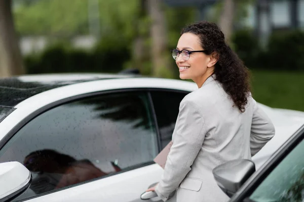 Heureuse femme d'affaires afro-américaine à lunettes regardant loin sur le parking — Photo de stock